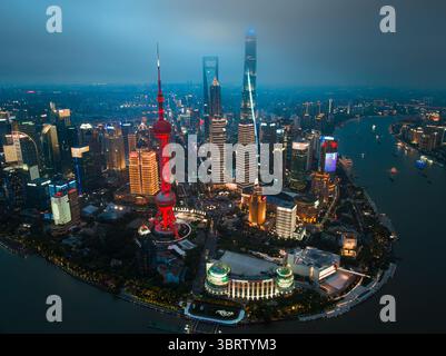 Shanghai, Cina - 21 giugno 2025: Veduta aerea della Oriental Pearl Tower illuminata e dei grattacieli torreggianti che piergono attraverso il cielo crepuscolo lungo il fiume Huangpu. Foto Stock