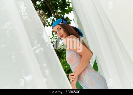 Una giovane donna si trova aggraziatamente all'aperto sotto gli alberi, abbracciando il calore della luce solare estiva. Foto Stock