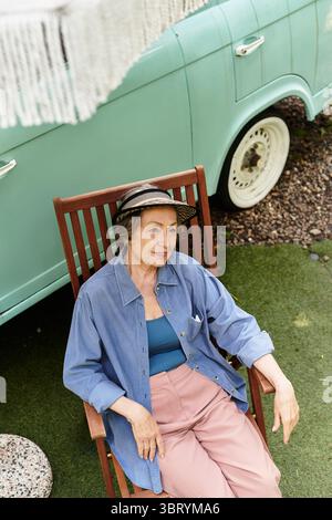 Una donna anziana si rilassa nel suo giardino, prendendo il sole seduto comodamente. Foto Stock