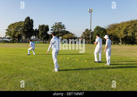Diversi compagni di squadra maschili di cricket in divise bianche che praticano esercitazioni sul campo con coni gialli Foto Stock