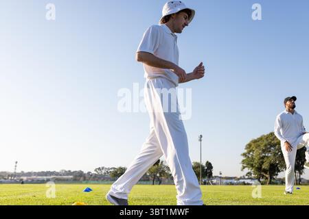 Diversi compagni di squadra maschi che camminano accanto ai coni sul campo di cricket vicino al palo luminoso in bianco, spazio copia Foto Stock