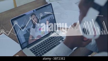 Uomo che ascolta con cuffie sovrauricolari, visualizza la tabella sul laptop alla scrivania con notebook, documenti Foto Stock