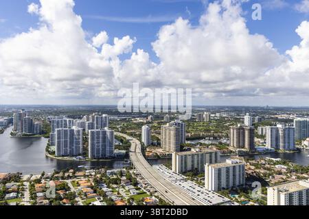 Vista aerea di alti edifici che riflettono il cielo luminoso, alti tra i corsi d'acqua e la vegetazione lussureggiante, Sunny Isles Beach, Florida, Stati Uniti. Foto Stock