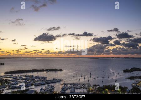 Vista aerea delle barche che costellano l'acqua nei pressi di un porticciolo sotto un cielo che si illumina con le sfumature ardenti del tramonto, Miami, Florida, Stati Uniti. Foto Stock