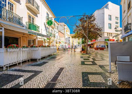 Una strada pittoresca con i tradizionali modelli portoghesi di pavimentazione e caffetterie sul marciapiede a Lagos, Portogallo, nella regione dell'Algarve. Foto Stock