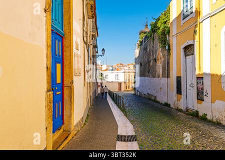 Le strette stradine acciottolate oltrepassano porte colorate ed edifici nel quartiere medievale Alfama di Lisbona, Portogallo. Foto Stock
