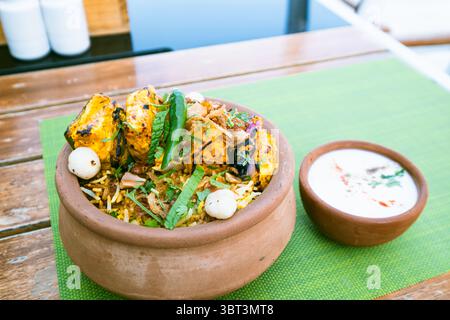 Tikka biryani paneer in un piatto di terra con raita di yogurt su un tovagliolo sul tavolo, sfondo fotografico di cucina indiana Foto Stock