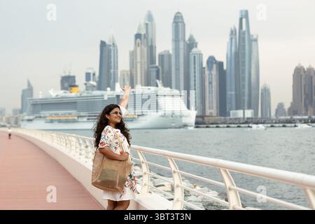 Turista donna che si gode la vista dello skyline di Dubai Marina con crociera sullo sfondo, solo viaggio economico a Dubai Foto Stock