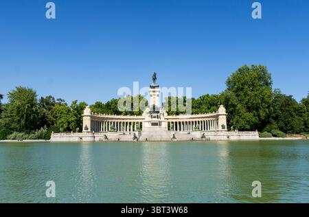 Il Monumento ad Alfonso XII nel Parco El Retiro di Madrid, che si riflette sul tranquillo stagno del Retiro sotto un cielo azzurro, un simbolo spagnolo senza tempo Foto Stock