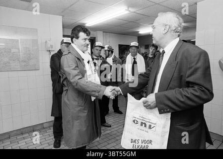 Mastenbroek (CNV) e Schalkx (FNV), Whizgle News, Dutch Desk, Paesi Bassi, 1950 - 2000 il 17-04-1991. Questi sono gli argomenti nell'immagine. In un vivace ambiente interno, diverse persone si riuniscono, vestite con abbigliamento formale, suggerendo un evento o una riunione. Lo spazio e' caratterizzato da piastrelle mondane che si estendono attraverso il pavimento e le pareti, creando un'atmosfera che si sente sia utilitaria che occupata. Verso il primo piano, due uomini si impegnano in una stretta di mano, il che significa un momento di cameratismo o accordo. Un uomo indossa un cappotto lungo e una sciarpa, suggerendo un clima fresco o un Foto Stock