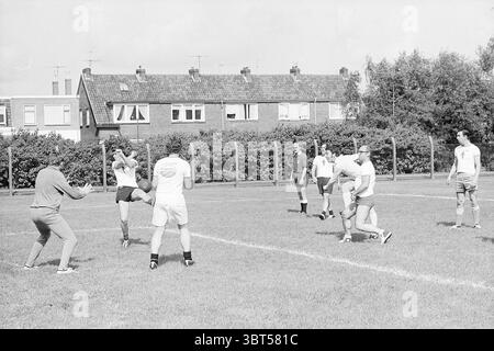 Le orchestre giocano calcio, Whizgle News, Dutch Desk, Paesi Bassi, 1950 - 2000 on 29-08-1969. Questi argomenti vengono visualizzati nell'immagine. In un campo erboso, un gruppo di individui è impegnato in una pratica di calcio giocosa. L'ambiente è luminoso e aperto, con uno sfondo di case della metà del secolo che mostrano una varietà di stili di finestre, alcune con tende che ondeggiano dolcemente nella brezza. Il cielo sovrastante è un grigio tenue, che suggerisce una giornata coperta, che conferisce alla scena un'atmosfera calma e soffusa. I partecipanti, vestiti con abbigliamento sportivo di vario tipo, esibiscono un mix di colori, alcuni rivestiti di pantaloncini bianchi Foto Stock