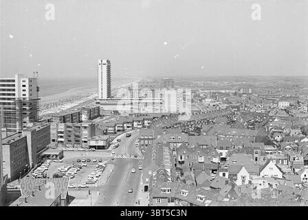 Overview Zandvoort Zandvoort, Whizgle News, Dutch Desk, Paesi Bassi, 1950 - 2000 il 04-07-1969. L'immagine contiene questi argomenti. La scena cattura un'ampia vista aerea di una città costiera, mostrando una miscela di elementi urbani e naturali. In primo piano, una serie di edifici residenziali densamente popolati mostrano un caratteristico stile architettonico con tetti a spiovente, molto probabilmente mattoni o piastrelle, creando un motivo testurizzato contro il cielo. Gli edifici variano in altezza e design, aggiungendo profondità alla composizione. Spostandosi verso la sezione centrale, la strada si snoda attraverso il paesaggio urbano, Foto Stock