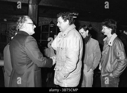 Ricevimento d'addio Mr. Blokker HD Haarlems Dagblad ecc. e IJmuider Courant e Koeri, Whizgle News, Dutch Desk, Paesi Bassi, 1950 - 2000 al 14-02-1986. Questi sono gli argomenti nell'immagine. In uno spazio interno scarsamente illuminato, un gruppo di persone si impegna nella conversazione, creando una scena che bilancia il calore con un pizzico di formalità. L'ambiente presenta travi di legno in alto e un caldo sfondo in mattoni, che contribuisce a creare un'atmosfera invitante. In prima linea, due uomini stringono la mano. Una, vestita con un abito scuro sartoriale, trasuda un'aria di professionalità e fiducia. L'altro, indossato Foto Stock