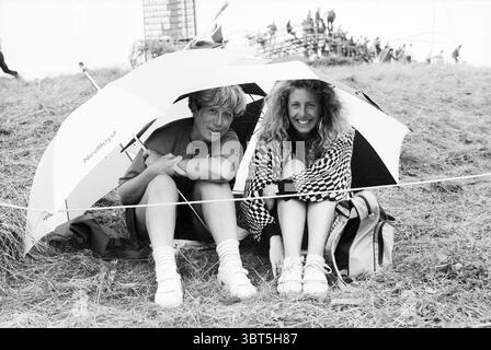 KLM apre varie registrazioni Golf Golf Golf 29-07-1989, Whizgle News, Dutch Desk, Paesi Bassi, 1950 - 2000 il 30-07-1989. Questi sono gli elementi dell'immagine. In un ambiente erboso all'aperto, due persone siedono vicino sotto un grande ombrello bianco, creando un angolo intimo e riparato. Il terreno è un mix di marrone chiaro e verde, che riflette il terreno naturale. Le due persone sono posizionate fianco a fianco, con le gambe incrociate davanti a loro. La persona sulla sinistra ha i capelli corti, un'espressione rilassata, ed è vestita con camicia e pantaloncini casual grigi. A destra, la seconda persona ha V Foto Stock