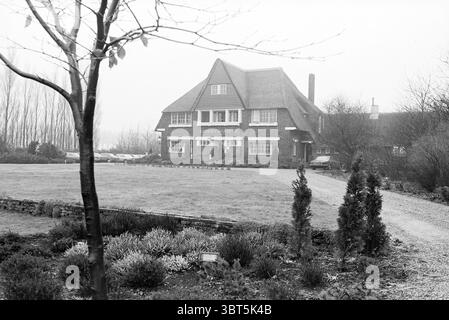 Pranzo introduttivo al ristorante "Alliance Gastronomique Néerlandaise" Inter Scaldes Kruiningen, Whizgle News, Dutch Desk, Paesi Bassi, 1950 - 2000 al 28-01-1981. Questi sono gli elementi dell'immagine. La scena raffigura una grande casa a due piani caratterizzata dalla sua architettura distinta. Presenta un tetto ripido e inclinato adornato con tegole e prominenti finestre dormitori che sbirciano fuori dal livello superiore. L'esterno e' fatto di mattoni, che conferiscono un aspetto robusto, mentre le finestre, incorniciate in bianco, creano un contrasto con la facciata piu' scura. Intorno alla casa c'è un ampio prato, che è un Foto Stock