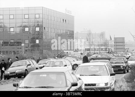 Grande interesse e asta pubblica di Troostwijk., Whizgle News, Dutch Desk, Paesi Bassi, 1950 - 2000. L'immagine mostra questi argomenti. La composizione raffigura un vivace ambiente urbano caratterizzato da una lunga fila di auto parcheggiate che costeggiano il lato di una strada. Questi veicoli, che variano nei modelli e nei colori, presentano per lo più toni tenui, con sfumature di bianco, grigio e nero predominanti, contribuendo a creare un'atmosfera un po' cupa. Sullo sfondo, un edificio moderno si erge alto, con la sua facciata composta da grandi pannelli di vetro che riflettono la luce soffusa di un cielo coperto. Le linee eleganti dell'edificio Foto Stock