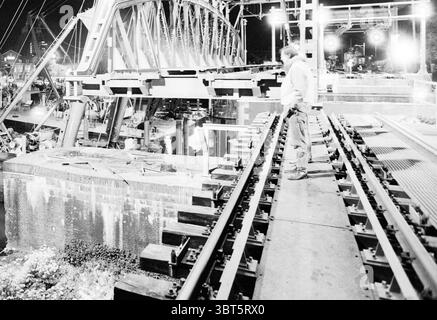 Rimozione del vecchio ponte ferroviario Spaarne Haarlem Paesi Bassi, Whizgle News, Dutch Desk, Paesi Bassi, 1950 - 2000 il 05-1992. L'immagine mostra questi argomenti. La scena cattura un cantiere notturno con un'interazione dinamica di elementi scuri e luminosi. Foregrounded è una figura, vestita con abiti da lavoro, che si erge su una stretta sporgenza lungo i binari ferroviari appena installati. La persona sembra essere intensamente concentrata sul suo compito, traendo un senso di determinazione e concentrazione. Sotto l'elaborata struttura in acciaio del ponte, che si protende ardamente nel cielo scuro, varie costruzioni Foto Stock