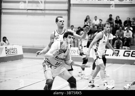 Akrides week Haarlem Paesi Bassi, Whizgle News, Dutch Desk, Paesi Bassi, 1950 - 2000 il 07-04-1992. Questi argomenti sono mostrati nell'immagine. La scena raffigura una partita di pallacanestro al coperto, che mostra un momento dinamico sul campo. In primo piano, due giocatori sono coinvolti in modo prominente, incarnando concentrazione e prontezza. Un giocatore, vestito con un'uniforme di colore chiaro con strisce larghe, è posizionato in basso, come se si preparasse a fare una mossa. Il suo obiettivo è intenso, muscoli pronti, suggerendo uno spirito competitivo. Ha i capelli corti e mostra un aspetto di determinazione, pronto a reagire al gioco u Foto Stock