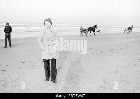 Andersson sulla spiaggia Wijk aan Zee Chess Wijk aan Zee, Whizgle News, Dutch Desk, Paesi Bassi, 1950 - 2000 il 24-01-1983. L'immagine contiene questi argomenti. In questa scena costiera, il primo piano presenta un giovane in piedi su una spiaggia di sabbia. Indossano un cappotto di colore chiaro e pantaloni scuri, i loro capelli infilati dal vento. La postura dell'individuo è rilassata, ma c'è un accenno di autocoscienza mentre guardano leggermente da un lato all'altro. Dietro di loro, si vedono un paio di persone. Un individuo sta con le spalle allo spettatore, rivestito di abiti scuri, suggerendo un contemplativo o un dista Foto Stock