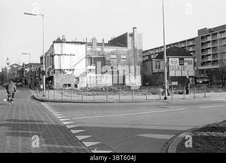 Cantiere Stationsplein Beverwijk Sites, Whizgle News, Dutch Desk, Paesi Bassi, 1950 - 2000 il 19-01-1976. Questi sono gli elementi dell'immagine. La scena cattura un ambiente urbano con un'attenzione particolare a un edificio parzialmente demolito sulla sinistra. La struttura appare intemprata, con mattoni esposti e sezioni dove la facciata è crollata. I resti delle pareti creano un netto contrasto contro il cielo, che è privo di nuvole, suggerendo una luce diurna brillante. A destra, sullo sfondo si infila un moderno complesso di appartamenti, caratterizzato da finestre rettangolari uniformi, che valorizzano il Foto Stock