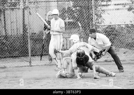 Softball Terrasvogels-Bloemendaal, Whizgle News, Dutch Desk, Paesi Bassi, 1950 - 2000 il 29-05-1992. Questi argomenti vengono visualizzati nell'immagine. La scena cattura un momento dinamico in una partita di baseball, ambientata su un campo sterrato racchiuso da una recinzione a catena. L'atmosfera è carica di emozioni, mentre i giocatori sono impegnati in azioni critiche. In primo piano, un giocatore, rivestito di un casco bianco e di una maglia, sta scivolando nel piatto di casa. La sua postura indica un mix di determinazione e urgenza, con sporcizia che lo circonda, evidenziando l'intensità del gioco. Dietro di lui, il ricevitore, che indossa un petto di petto Foto Stock