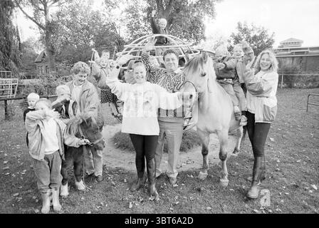 Animal Day Playground Children's Joy, Whizgle News, Dutch Desk, Paesi Bassi, 1950 - 2000 il 03-10-1990. Questi sono gli elementi dell'immagine. La scena è vivace e divertente, catturando un gruppo di bambini e adulti in un ambiente dinamico all'aperto. Un grande e intricato parco giochi, simile a una struttura di arrampicata, è centrale nella composizione, con diversi bambini gioiosamente arroccati in cima, la loro eccitazione evidente nelle loro espressioni e postura. In primo piano, una donna sta accanto a un cavallo, le sue braccia sollevate in una posa allegra, irradiando un senso di gioia e impegno con il bambino Foto Stock