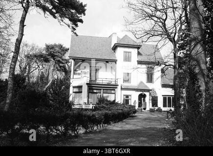 Esterno villa Denheim Bloemendaal, Whizgle News, Dutch Desk, Paesi Bassi, 1950 - 2000 il 24-03-1993. Questi sono gli elementi dell'immagine. La scena presenta una grande casa a due piani con uno stile architettonico distinto, caratterizzata da un tetto spiovente e da grondaie decorative. L'esterno e' dipinto in una tonalità chiara, in contrasto con le sfumature piu' scure del verde circostante. La casa è incorniciata da un prato curato, punteggiato da cespugli e piccoli alberi che aggiungono profondità al paesaggio. A sinistra, gli alti pini si allungano verso l'alto, con le loro silhouette scure che forniscono un cont Foto Stock
