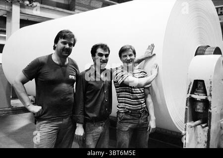 Relazione della fabbrica di carta Gelder Velsen-Noord Van Gelder & Zonen Velsen-Noord, Whizgle News, Dutch Desk, Paesi Bassi, 1950 - 2000 il 27-01-1983. L'immagine mostra questi argomenti. La scena raffigura tre uomini in piedi insieme in un ambiente industriale, caratterizzato da un grande rotolo di carta bianca dietro di loro. Gli uomini sono posizionati in primo piano, ognuno con espressioni e posture distinte che suggeriscono cameratismo e orgoglio nel loro ambiente di lavoro. L'uomo a sinistra indossa una camicia scura e la sua posizione rilassata e il suo leggero sorriso indicano un comportamento amichevole. Foto Stock