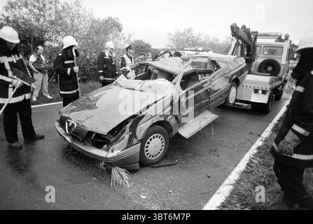 Incidente Zeeweg B'daal Bloemendaal Zeeweg, Whizgle News, Dutch Desk, Paesi Bassi, 1950 - 2000 il 07-09-1994. Questi sono gli elementi dell'immagine. La scena raffigura un momento cupo su una strada rurale. In primo piano, un veicolo gravemente danneggiato occupa il centro, la sua carrozzeria è deformata e le sezioni mancanti, rivelando l'interno e i resti di vetro frantumato. I colori della vettura, principalmente scuri e silenziosi, contrastano nettamente con il verde che la circonda. Da un lato, diversi membri del personale del servizio di emergenza sono impegnati nei loro compiti, indossando uniformi standard composte da nero e rif Foto Stock