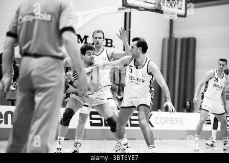 Akrides week Haarlem Paesi Bassi, Whizgle News, Dutch Desk, Paesi Bassi, 1950 - 2000 il 07-04-1992. Questi sono gli argomenti nell'immagine. La scena cattura un momento intenso da una partita di basket. Un gruppo di giocatori è impegnato sul campo, mostrando uno spettro di atletismo e strategia. In primo piano, due atleti sono bloccati in una gara per il posizionamento. Uno, vestito con un'uniforme scura, sembra che stia tentando di guidare verso il cesto, il suo corpo basso e pronto per una manovra. L'altro giocatore, indossando una maglia bianca impreziosita da un numero, è fermo, pronto a difendersi Foto Stock