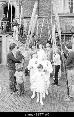 Coppia nuziale Lambert scout in barca di fronte al municipio Wedding, Whizgle News, Dutch Desk, Paesi Bassi, 1950 - 2000 il 21-12-1983. Questi sono gli elementi dell'immagine. In una vivace scena all'aperto, domina un'atmosfera gioiosa e celebrativa. L'ambiente sembra essere di fronte ad un edificio storico, evidente dai suoi dettagli architettonici, con una grande scalinata che conduce ad una serie di grandi porte. In primo piano, diversi bambini vestiti con abiti bianchi e voluminosi, che assomigliano all'abbigliamento tradizionale spesso visto durante i matrimoni, guidano la strada. Le loro espressioni sono brillanti e allegre, aggiungendo Foto Stock
