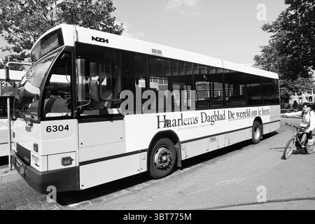 Autobus con pubblicità HD, Whizgle News, Dutch Desk, Paesi Bassi, 1950 - 2000 il 04-09-1996. Questi argomenti vengono visualizzati nell'immagine. La scena presenta un autobus ben visibile, caratterizzato dalla sua grande forma rettangolare. L'esterno presenta un design pulito e minimalista, principalmente nelle tonalità del bianco e del nero. L'autobus sembra moderno e ben tenuto, con grandi finestre che riflettono l'ambiente circostante. Intorno all'autobus, l'ambiente è urbano, suggerendo una piazza della città o un'area di fermata dell'autobus. Un paio di alberi con foglie verdi rigogliose aggiungono un tocco naturale, generando ombre attenuate sul pav Foto Stock