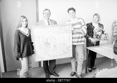 Cerimonia di premiazione della classe sul giornale, Whizgle News, Dutch Desk, Paesi Bassi, 1950 - 2000 il 05-11-1992. L'immagine contiene questi argomenti. Si sta svolgendo un incontro in un ambiente interno luminoso e semplice. La luce naturale entra dalla finestra, proiettando una luce soffusa sulla scena e creando un'atmosfera calda. A sinistra, una giovane donna sorride, indossa un maglione oversize scuro con un profondo scollo a V. I suoi lunghi capelli cadono sulle spalle, incorniciando il suo viso. Possiede un lato di una grande opera d'arte, che sembra essere il punto focale di questo raduno. Il piec Foto Stock