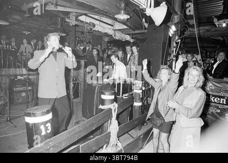 Serata gastronomica deliziosa con accompagnamento musicale presso il centro bowling Claus e la sala da festa Haarlem Orionweg Paesi Bassi, Whizgle News, Dutch Desk, Paesi Bassi, 1950 - 2000 al 31-10-1993. Questi sono gli elementi dell'immagine. In una vivace scena al chiuso, l'atmosfera è piena di energia, mentre un artista è in prima linea, gestendo con passione con un microfono in mano. È vestito con un abito brillante, in contrasto con l'ambiente più scuro. Dietro di lui, un piccolo gruppo di persone gestisce l'apparecchiatura audio, concentrandosi e impegnandosi con la musica. Il pubblico, visibile nel backgr Foto Stock