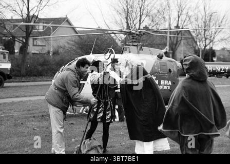 Saint Nicholas in elicottero Nieuw-Vennep Nieuw-Vennep, Whizgle News, Dutch Desk, Paesi Bassi, 1950 - 2000 il 02-12-1993. Questi argomenti vengono visualizzati nell'immagine. In una scena piena di curiosità ed eccitazione, un gruppo di persone è radunato all'aperto, apparentemente in un parco o in un'area aperta. Lo sfondo presenta un elicottero e le sue pale rotore che creano un punto focale sorprendente. L'aereo siede sull'erba, dipinto in un colore scuro, accentuato da un emblema d'argento, che indica il suo scopo operativo. In primo piano, un uomo vestito con un abbigliamento casual, possibilmente un cappotto e un jeans, è impegnato con t Foto Stock