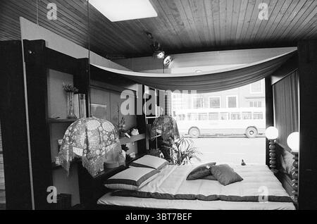 Interni di Van Duijvenboden interni Haarlem Gedempte Oude Gracht 90 Paesi Bassi, Whizgle News, Dutch Desk, Paesi Bassi, 1950 - 2000 il 28-03-1973. L'immagine include questi argomenti. La scena presenta una camera da letto splendidamente arredata che trasuda un'atmosfera tranquilla e minimalista. Il letto, accoccolato in primo piano, ha un design semplice ma invitante, caratterizzato da un materasso ben disposto con due grandi cuscini e un cuscino decorativo in una tenue ombra. Sopra il letto, un morbido baldacchino che scorre drappa graziosamente dal soffitto, aggiungendo un elemento di eleganza. I muri sono ado Foto Stock