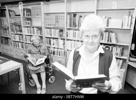 Sig.ra @@n Velserduin Driehuis Driehuis Nicolaas Beetslaan, Whizgle News, Dutch Desk, Paesi Bassi, 1950 - 2000 al 25-02-1991. Questi argomenti vengono visualizzati nell'immagine. In una biblioteca molto illuminata, due donne anziane sono impegnate con i libri, creando un'atmosfera intima. Lo sfondo è costituito da ripiani in legno traboccanti di libri ben organizzati, prevalentemente in colori tenui come beige e marrone chiaro, contribuendo a creare un ambiente accogliente. In primo piano, una donna con capelli bianchi e morbidi e occhiali si concentra su un libro, la sua espressione un mix di curiosità e concentrazione. E' vestita con un colore chiaro Foto Stock
