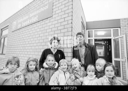 Director Schools V'Broek Velserbroek, Whizgle News, Dutch Desk, Paesi Bassi, 1950 - 2000 il 31-01-1991. L'immagine mostra questi argomenti. La scena presenta un gruppo di bambini, prevalentemente ragazze, riuniti da vicino davanti ad un edificio in mattoni. I bambini, vestiti con giacche invernali, mostrano una serie di espressioni, dai sorrisi timidi ai grins allegri. I loro outfit sono caratterizzati da vari colori tenui, che riflettono una giornata fresca e ricoperta. A sinistra e a destra dei bambini si trovano due adulti, probabilmente educatori o operatori sanitari. Un adulto ha i capelli ricci e indossa una camicetta a motivi geometrici, mentre l'altro Foto Stock