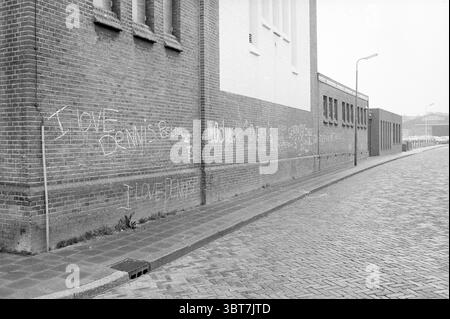 Testi su [Adelbertus e] Engelmunduskerk IJmuiden Churches Texts IJmuiden Koningin Wilhelminakade Paesi Bassi, Whizgle News, Dutch Desk, Paesi Bassi, 1950 - 2000 il 06-06-1985. L'immagine include questi argomenti. La scena presenta un tranquillo angolo urbano di strada, dove un muro di mattoni testurizzati forma lo sfondo della composizione. Il muro, prevalentemente in calde tonalità di rosso e marrone, è segnato da scritti di gesso bianco che esprimono messaggi di affetto e sentimento. Il testo, un po' sbiadito e irregolare, si intreccia sulla superficie, suggerendo storie personali o espressioni locali. Alla l Foto Stock