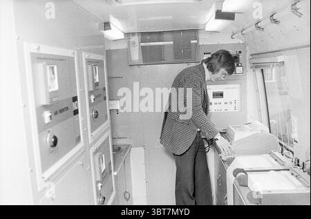 Veicolo di misurazione dell'inquinamento atmosferico, Whizgle News, Dutch Desk, Paesi Bassi, 1950 - 2000 il 21-03-1974. L'immagine include questi argomenti. La scena si svolge all'interno di uno spazio compatto e chiuso che assomiglia a un'unità mobile o a un furgone. Le pareti sono principalmente di colore chiaro, offrendo un'atmosfera neutra e sterile. Sul lato sinistro, diversi armadi o pannelli metallici sono disposti in modo ordinato, ciascuno con una serie di pulsanti e quadranti, suggerendo che possono controllare varie funzioni dell'unità. Al centro, una persona è attivamente impegnata con un'attrezzatura posizionata su un bancone. Questo individuo lo è Foto Stock