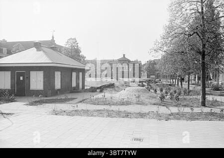 Panoramica Leidscheplein Haarlem Overviews Square Haarlem Leidseplein Paesi Bassi, Whizgle News, Dutch Desk, Paesi Bassi, 1950 - 2000 il 18-05-1976. L'immagine contiene questi argomenti. La scena presenta un tranquillo ambiente urbano con un edificio solitario sulla sinistra, caratterizzato da un tetto inclinato e una facciata semplice adornata da finestre a bordo. Questa struttura appare un po' intemprata, suggerendo un'età che si fonde con l'ambiente circostante. A destra è visibile un'area sabbiosa, possibilmente un parco pubblico o un cantiere, con macchie di terra irregolari e vegetazione sparsa. Qualche giovane albero Foto Stock