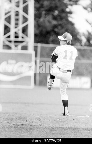 Australia - Japan Baseball, Whizgle News, Dutch Desk, Paesi Bassi, 1950 - 2000 il 14-08-1978. L'immagine include questi argomenti. In questa scena, un giovane atleta viene catturato in un momento dinamico su un campo da baseball. Il giocatore, vestito con una classica uniforme caratterizzata da un tessuto bianco lucido con dettagli in blu navy, si erge sul tumulo del lanciatore. La sua posizione è pronta, una gamba sollevata in alto con un movimento di lancio, dimostrando sia la concentrazione che l'atletismo. Lo sfondo mostra una visione sfocata del campo da baseball, con una recinzione a catena e una grande pubblicità parzialmente visibile, aggiungendo contesto ai setti Foto Stock