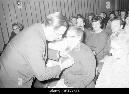 Onorare la signora Stoutenbeek Croce Rossa Croce Rossa Croce Rossa ospedale, Whizgle News, Dutch Desk, Paesi Bassi, 1950 - 2000 il 14-11-1967. Questi sono gli elementi dell'immagine. La scena cattura un incontro di persone sedute in un auditorium poco illuminato, creando un'atmosfera intima e concentrata. L'ambientazione suggerisce un evento formale, possibilmente una cerimonia o una presentazione, con file di partecipanti che sono seduti a stretto contatto, le loro espressioni riflettono un mix di attenzione e anticipazione. In primo piano, un uomo vestito con un abito scuro si piega leggermente verso una donna più anziana, che indossa il vetro Foto Stock