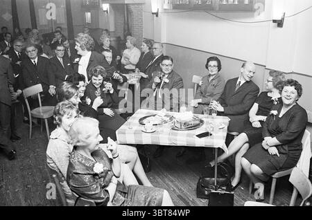 Giubileo 60 anni. Associazione ciclistica De Kampioen ricevimenti Ciclismo Haarlem Rijksstraatweg Paesi Bassi, Whizgle News, Dutch Desk, Paesi Bassi, 1950 - 2000 il 14-11-1965. L'immagine include questi argomenti. La scena si sviluppa in un ambiente interno che trasuda un senso di incontro sociale e di festa. La sala e' piena di un mix di individui ben vestiti, suggerendo un evento formale o una festa. In primo piano, un gruppo di donne occupa una tavola adornata con una tovaglia a scacchi, che aggiunge un tocco di calore e casualità all'atmosfera altrimenti formale. Queste donne, ogni wea Foto Stock