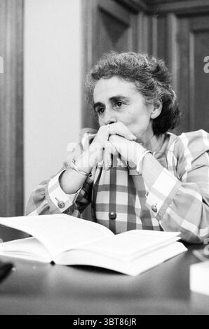 Ritratto di una donna con un libro sull'aborto nei Paesi Bassi, Whizgle News, Dutch Desk, Paesi Bassi, 1950 - 2000 il 10-1986. Questi sono gli elementi dell'immagine. La scena cattura una donna che appare profondamente nel pensiero, seduta a un tavolo con un libro aperto davanti a lei. I suoi capelli, un grigio leggermente ondulato, incorniciano il viso, che ha un'espressione penosa. È vestita con un'audace camicetta a scacchi caratterizzata da quadrati alternati di tonalità chiare e scure, che aggiungono un contrasto sorprendente all'ambiente più sobrio. Lo sfondo è costituito da pannelli in legno che contribuiscono ad una calda e intima a Foto Stock