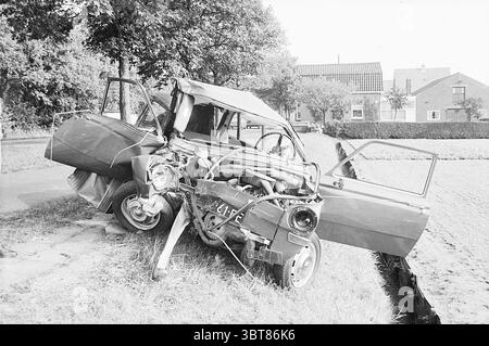 Whizgle News, Dutch Desk, Paesi Bassi, 1950 - 2000. L'immagine mostra questi argomenti. La scena raffigura un veicolo gravemente danneggiato posizionato lungo una strada rurale. La vettura sembra essere stata coinvolta in una collisione significativa, come dimostrato dal suo telaio anteriore deformato e inclinato. Una delle porte è aperta, rivelando un interno disordinato con detriti sparsi. La vettura è prevalentemente una tonalità opaca, forse blu o grigio sbiadito, completata dalla tonalità nera e bianca dell'impostazione generale. Intorno al veicolo è presente un'area di erba, lussureggiante e ricoperta di vegetazione, che contrasta con la Foto Stock