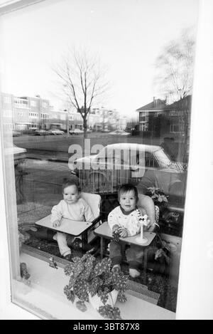 Gemelli davanti alla finestra Kleverlaan fam. Helversteyn Children's Homes Children's Party Children Twins Haarlem Kleverlaan Paesi Bassi, Whizgle News, Dutch Desk, Paesi Bassi, 1950 - 2000 il 27-12-1988. Questi argomenti sono mostrati nell'immagine. In un ambiente tranquillo, due bambini siedono fianco a fianco su seggioloni, affacciati su una grande finestra. I seggioloni sono posizionati contro il vetro ed entrambi i bambini mostrano un'espressione curiosa, guardando in avanti. Un bambino ha i capelli marrone chiaro ed è vestito con un vestito di colore chiaro, mentre l'altro ha i capelli più scuri e indossa un Foto Stock