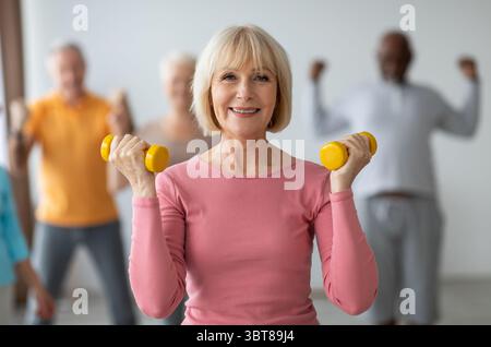 Signora anziana che fa l'allenamento di costruzione di resistenza con i dumbbells Foto Stock
