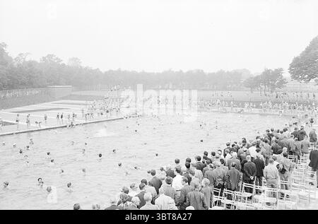 Apertura piscina Herenduinweg apertura aperture messo in uso IJmuiden Heerenduinweg Paesi Bassi, Whizgle News, Dutch Desk, Paesi Bassi, 1950 - 2000 il 17-06-1966. Questi argomenti sono mostrati nell'immagine. La scena si snoda in una vivace piscina all'aperto, piena di energia. La composizione cattura un grande raduno di persone, posizionato su entrambi i lati della piscina. Da un lato, una disposizione a più livelli di sedie in legno accoglie gli spettatori, che sembrano impegnati e animati, alcuni chiacchierano o puntano verso l'acqua. Nella piscina, una varietà di nuotatori portano in acqua, creando strappi Foto Stock