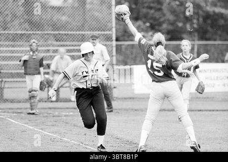 Softball: TYBB-DSC 74, Whizgle News, Dutch Desk, Paesi Bassi, 1950 - 2000 il 07-06-1997. Questi argomenti vengono visualizzati nell'immagine. In una scena sportiva dinamica, due giocatori sono impegnati in un momento di tensione sul campo. Un atleta, rivestito di una maglia grigia con la scritta "TYERS" stampata sul davanti, indossa un casco bianco e sta volando verso una base, mostrando determinazione e impegno. L'altro giocatore, vestito con una maglia rossa brillante con il numero "15", è posizionato difensivamente, pronto a ricevere un lancio. La sua espressione indica la concentrazione e la prontezza mentre si prepara a fare un gioco. Sullo sfondo, additio Foto Stock